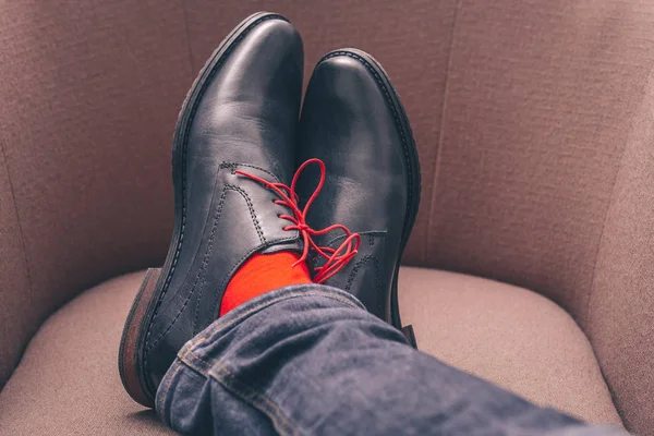 The legs of a man in shoes with red laces and in red stylish socks, fashionable shoes, a first-person view