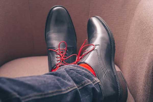 The man put his feet in classic leather shoes with red laces and in red stylish socks on a chair, a kind from the first person