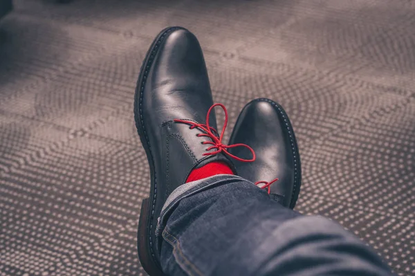 The legs of a man in shoes with red laces and in red socks are impressively thrown one on top of another, a kind from the first person