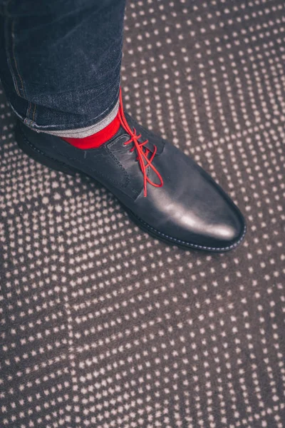 Leg of a man in classic leather shoes with red laces and in red stylish socks, fashion on shoes, first person view