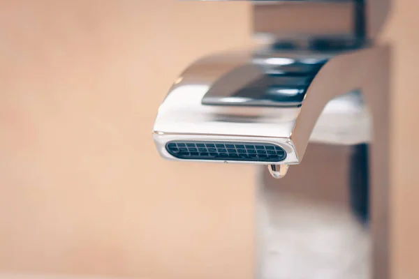 A drop hangs on the faucet in the bathroom, saving natural resources, saving water