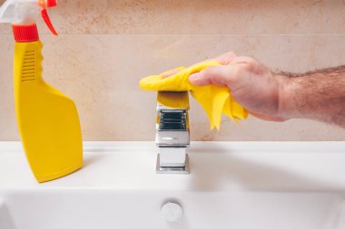 Bir adam banyoda yeni bir krom kaplama musluk bezi ile siliyor