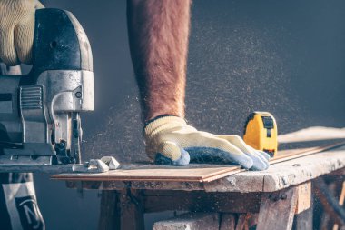 Testereden gelen talaş her yöne doğru uçuyor. İşçi yerleştirmek için laminatı kesiyor.