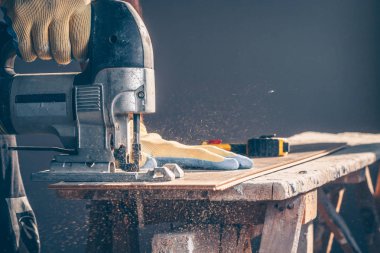 İşçi bir elektrikli jigsaw ile panoları kesiyor, toz her yöne uçar, maranboz