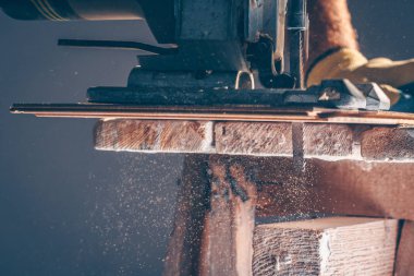 İşçi bir elektrikli jigsaw ile panoları kesiyor, toz her yöne uçar, maranboz