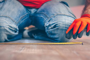 İnşaat ölçme bandı olan bir işçi, ahşap zemine ölçümler yapar