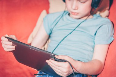 Kırmızı saçlı çocuk kanepede oturan oyun tablette oynuyor