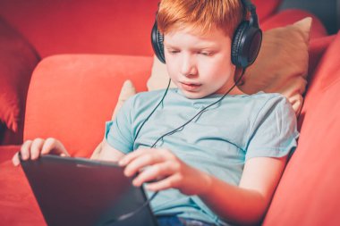 Bir tablet üzerinde bir film izlerken bir kanepede yatan Kızıl saçlı çocuk