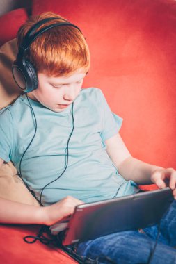 Kırmızı saçlı çocuk kanepede oturan oyun tablette oynuyor