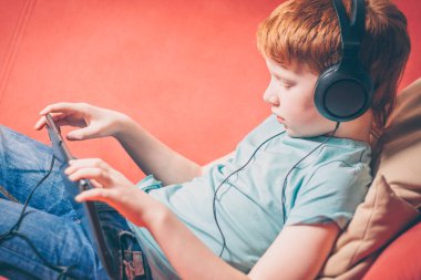 Bir tablet üzerinde bir film izlerken bir kanepede yatan Kızıl saçlı çocuk