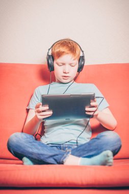 Kanepede oturan kırmızı saçlı çocuk tablette yabancı dil kursu dinlerken