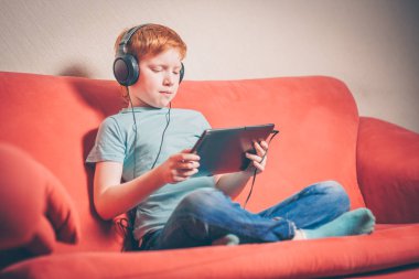 Kanepede oturan kırmızı saçlı çocuk tablette yabancı dil kursu dinlerken