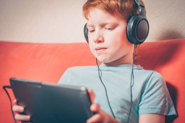 Kanepede oturan kırmızı saçlı çocuk tablette yabancı dil kursu dinlerken