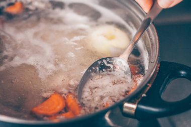 Bir kaşık ile Cook bir tencerede kaynar çorba köpük kaldırır