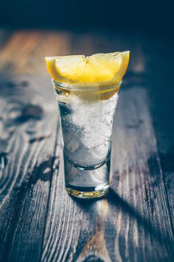 Buz gibi bir bardak votka ve bir dilim limon içeren ahşap rustik masa