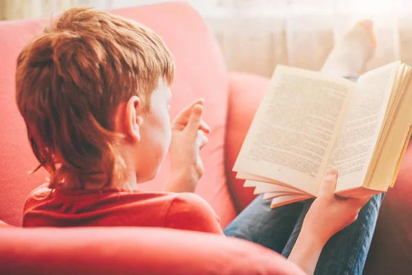 红头发的男孩舒适地坐在柔软的扶手椅上 背诵着读物中的一段话 — 图库照片
