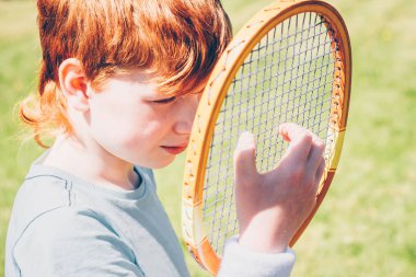 Kızıl saçlı çocuk tenis oyuncusu raket üzerindeki ızgaranın gerginliğini kontrol eder