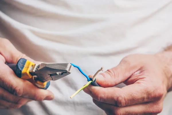 The electrician performs electrical work - clamps the cable with pliers