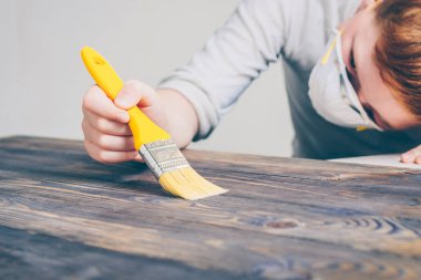 Bir boya fırçası ile yüz maskesi kırmızı saçlı çocuk ahşap bir yüzey boyar