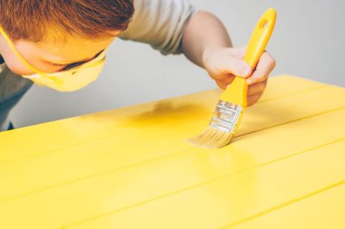 Bir boya fırçası ile Kızıl saçlı çocuk eski bir ahşap masada bir vernik uygulanan