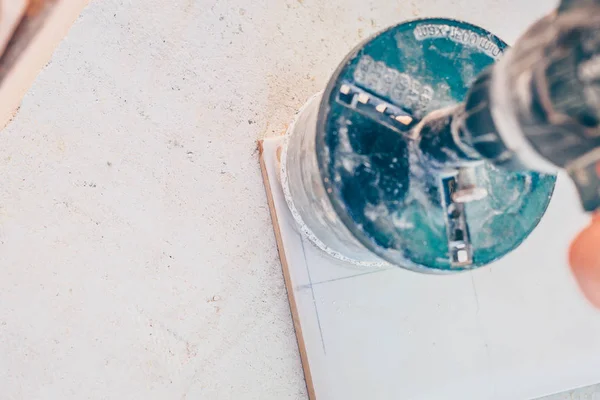 Finishing works - the worker cuts a round hole in the tile for mounting electricians with a screwdriver and a diamond bit