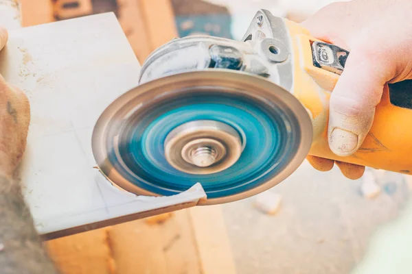 Finishing works - the tiler cuts a round hole in the tile with an angle grinder