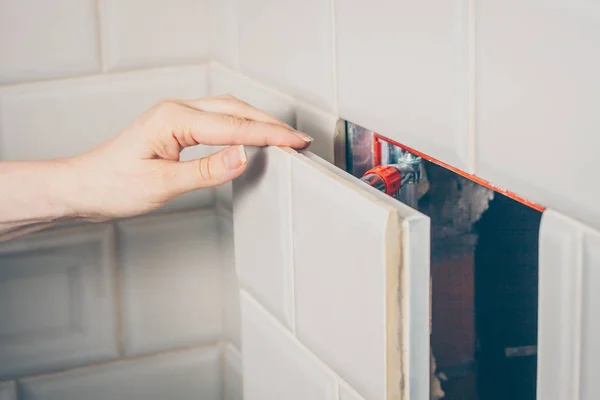 The girl opens a hidden hatch on the wall of the tile to access the inspection hole of the sewer pipe to eliminate clogging and cleaning