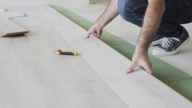 Bir işçi eli, panelleri bir kilitle birbirine bağlayan bir laminata vuruyor.