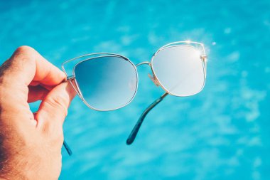 Havuzda parlak mavi su bir arka plan üzerinde elinde metal çerçeve güzel güneş gözlüğü