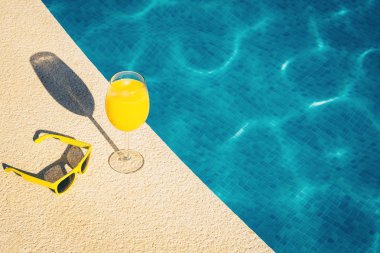 Yaz tatilinin özellikleri - güneş gözlüğü ve bir bardak meyve suyu - havuzun arka planında.