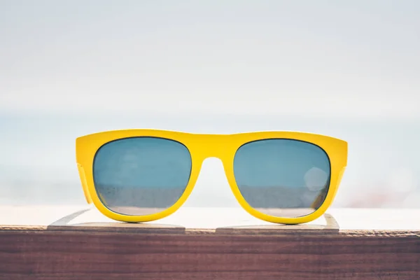 Sunglasses in yellow frame on a wooden board on the coast