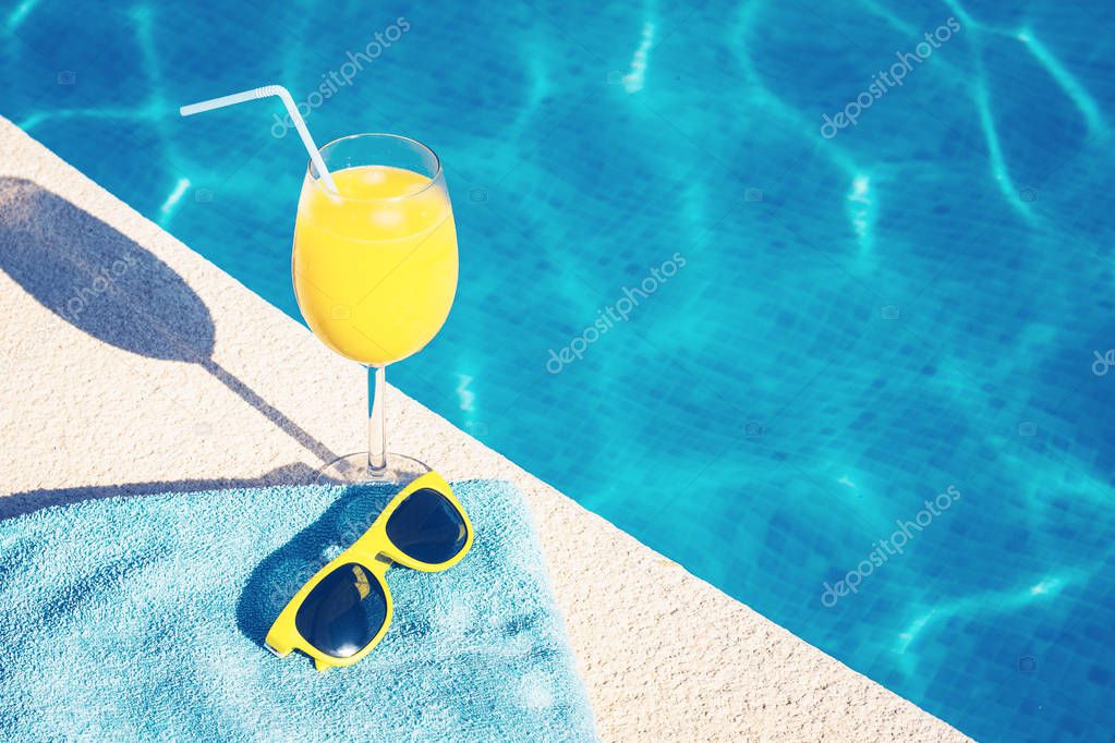 Attributes of summer vacation - sunglasses and a glass of juice - on the background of the pool