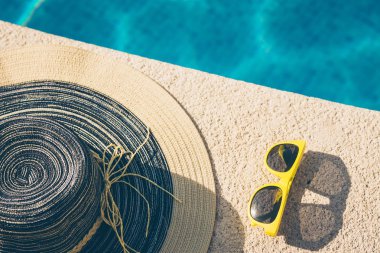 Sarı güneş gözlüğü, havuzun taştan tarafında bir şapka.