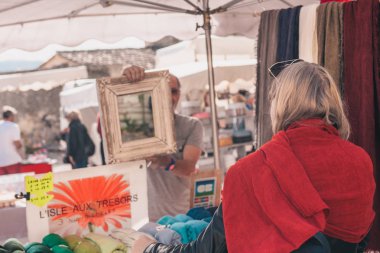 Gordes, Provence-Alpes-Cote d'Azur, Fransa, 25 Eylül 2018: Kız dükkanda bir atkı seçer ve satın alır - Provence geleneksel bir çiftçi pazarı