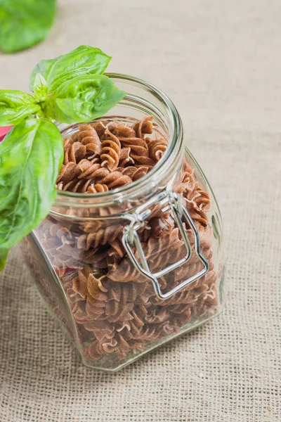 Close-up of fusilli pasta in a jar with a basil leaf on a linen cloth