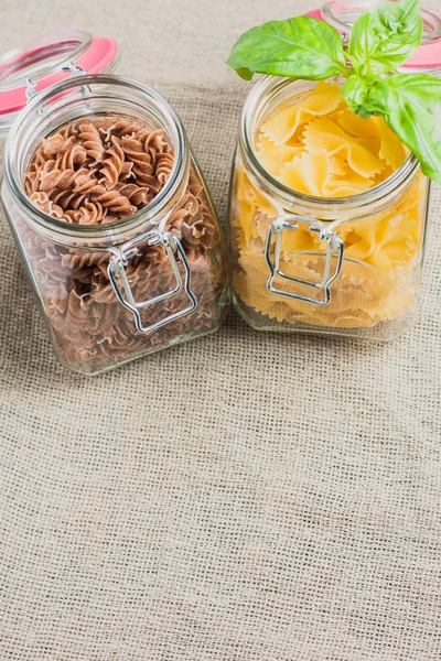 Close-up of farfalle pasta and fusilli in a jar with a leaf of basil on a linen cloth - copy space