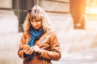 Kot pantolonlu ve deri ceketli bir kadın akıllı telefon navigatöründeki güzergaha bakıyor.