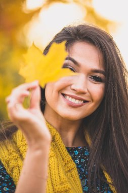 Sarı bir sonbahar akçaağaç yaprağı ile neşeli esmer - yüzünde mutlu bir gülümseme