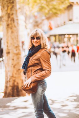 Çekici, zayıf, sarışın kadın güneşli bir caddede gülümsüyor.