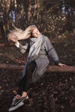 Sonbahar ormanında tatlı, seksi sarışın bir kütüğün üzerinde oturur ve rüzgarda saçlarıyla oynar.