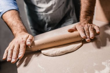 Bir fırıncı elleri ahşap bir oklava ile hamuru masanın üzerinde ince bir tabaka haline getirir.