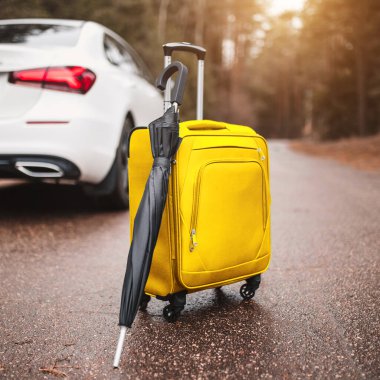 Sarı bavul ve şemsiye yolda beyaz bir arabanın yanında - araba yolculuğu için hazırlık
