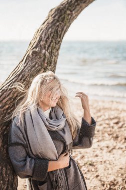 Rüzgarla savrulmuş uzun sarı saçlar neşeli sarışın bir kadının yüzünde - rüzgarlı bir günde deniz kenarında