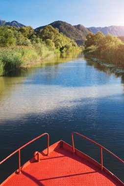Kırmızı teknenin pruvası nehir kanalının arka planına karşı - güneşli bir günde nehir yürüyüşü - sazlıklar arasındaki gölde seyahat eder
