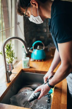 Minsk, Belarus - 20 Haziran 2020: Adam karısına yardım edip yemek hazırlıyor - mutfaktaki lavaboda balık temizliyor