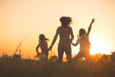 Uzakta günbatımı ve su bakan iki küçük kızı annesiyle silüeti