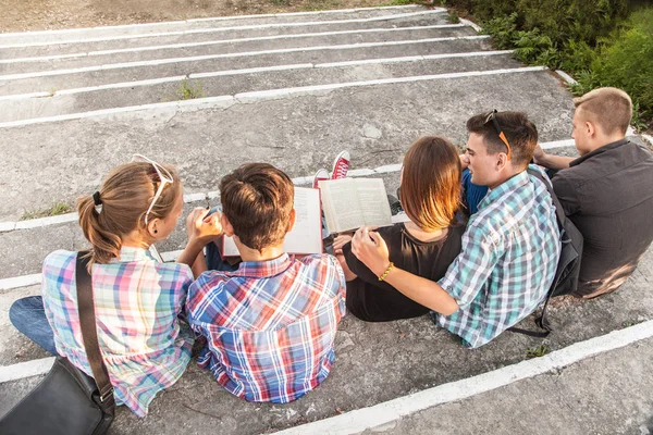 一群拿着书和小玩意的年轻学生坐在公园的台阶上 — 图库照片