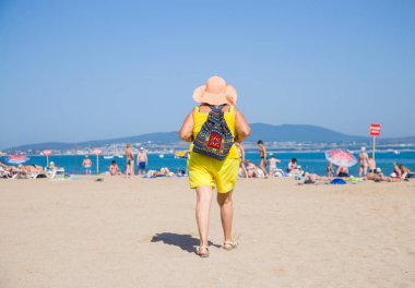 Yaşlı kadın beach's elbise ve şapka kumlu plaja denizde geliyor.