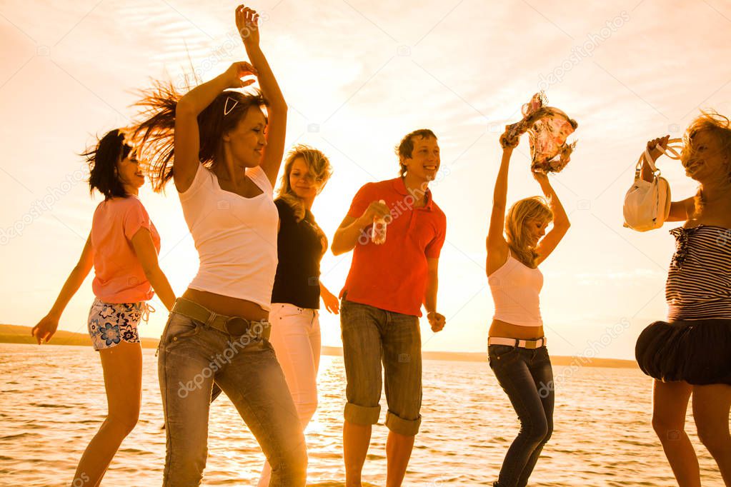 group of happy young people dancing at the beach on  beautiful summer sunset