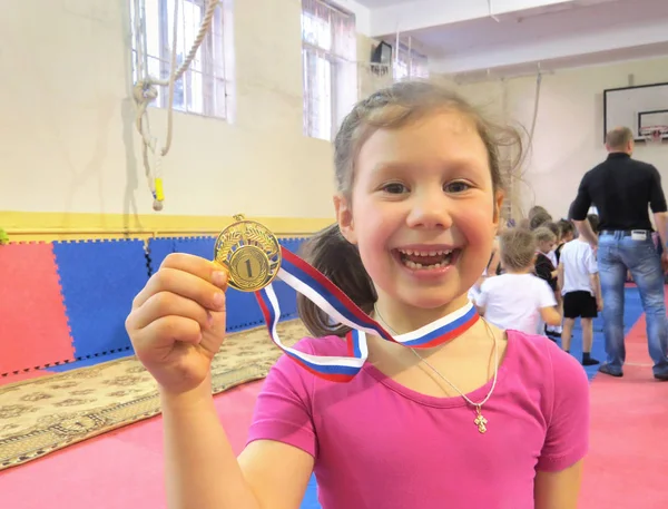 little girl shows gold medal for winning a gymnastics competition in the gym